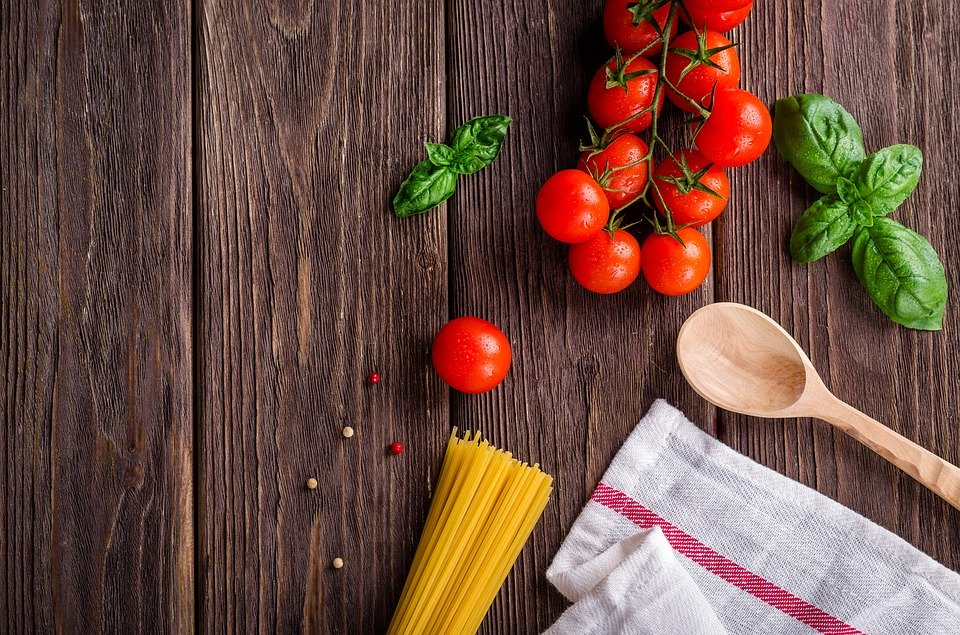 pasta, tomatoes, and basil laid out next to a kitchen towel and a wooden cooking spoon.